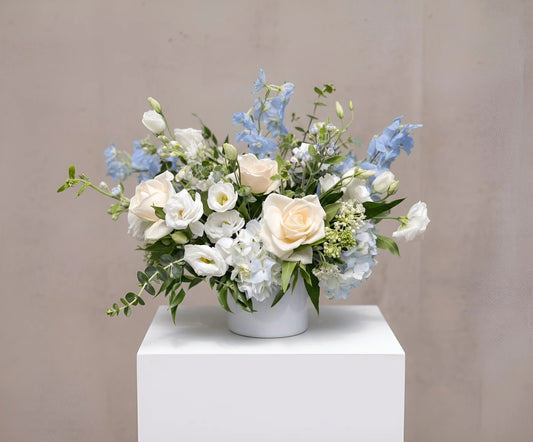 Floral arrangement with white and blue flowers in a white vase on a light gray background