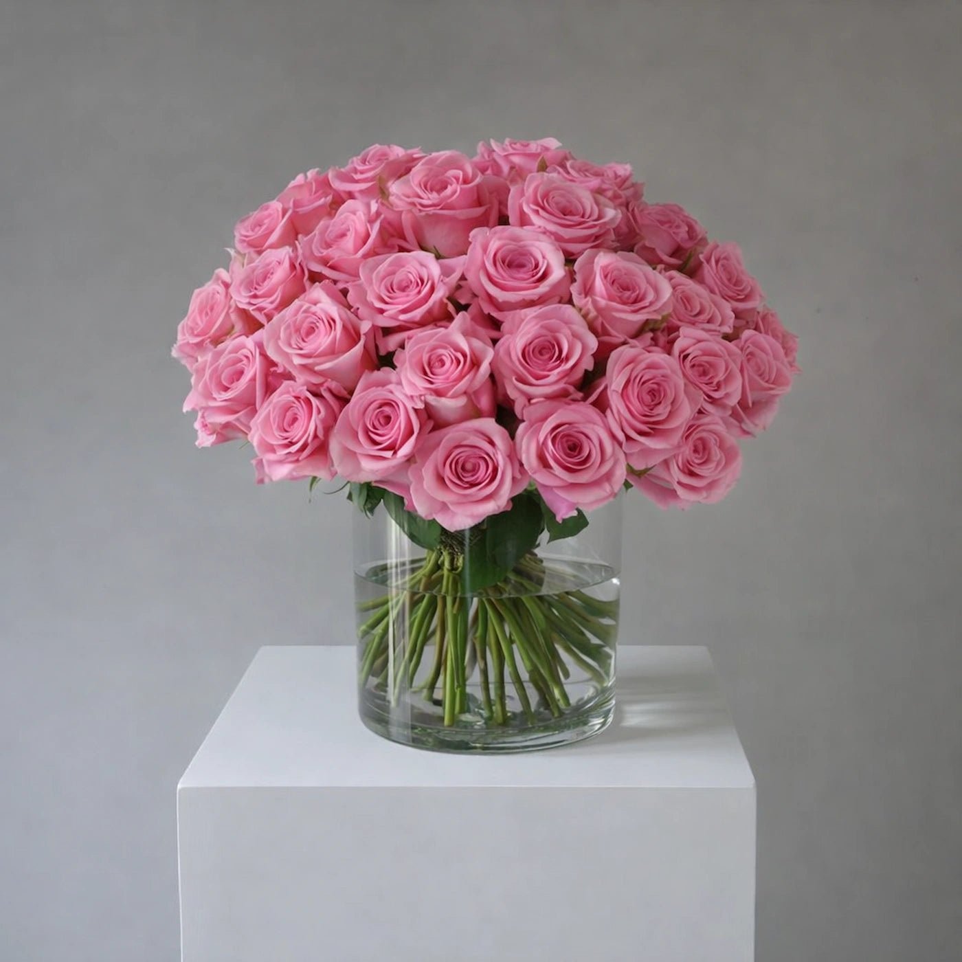 Bouquet of pink roses in a clear vase on a white pedestal against a gray background
