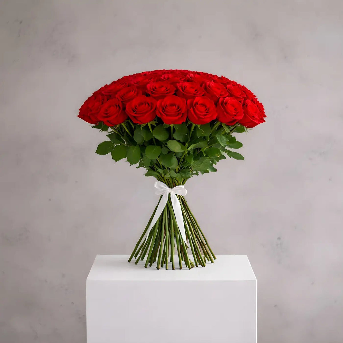 Bouquet of red roses on a white pedestal with a gray background