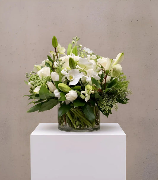 Bouquet of white and green flowers in a clear vase on a white pedestal against a beige background
