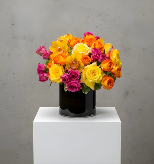 Colorful bouquet of flowers in a black vase on a white pedestal against a gray background