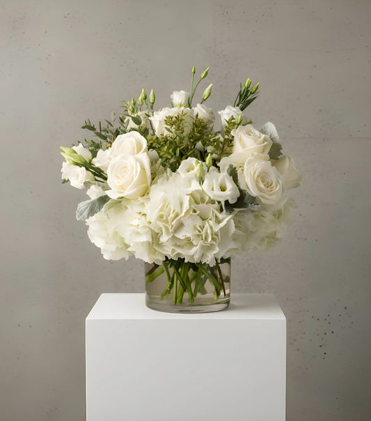 Bouquet of white flowers in a clear vase on a white pedestal against a gray background