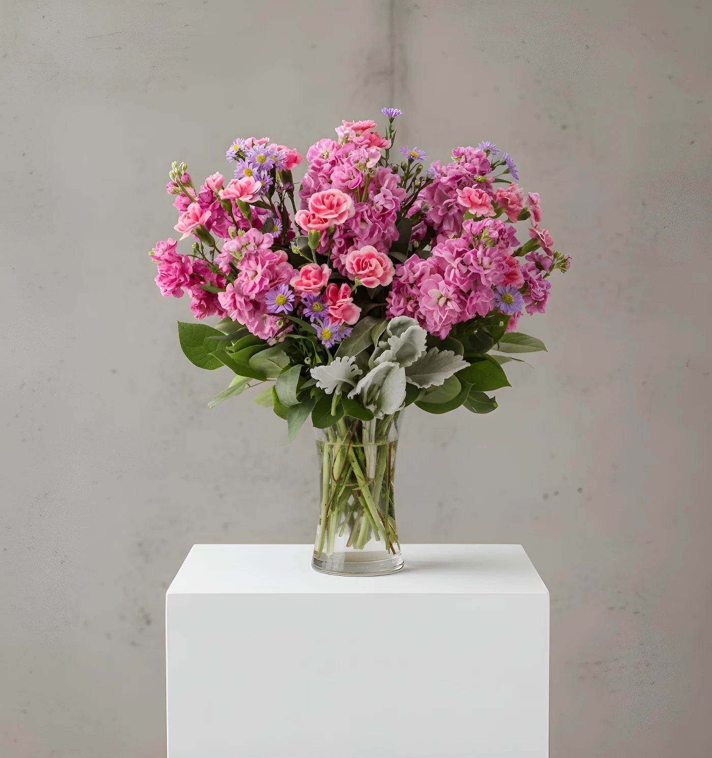 Bouquet of pink flowers in a clear vase on a white pedestal against a gray background