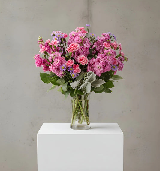 Bouquet of pink flowers in a clear vase on a white pedestal against a gray background