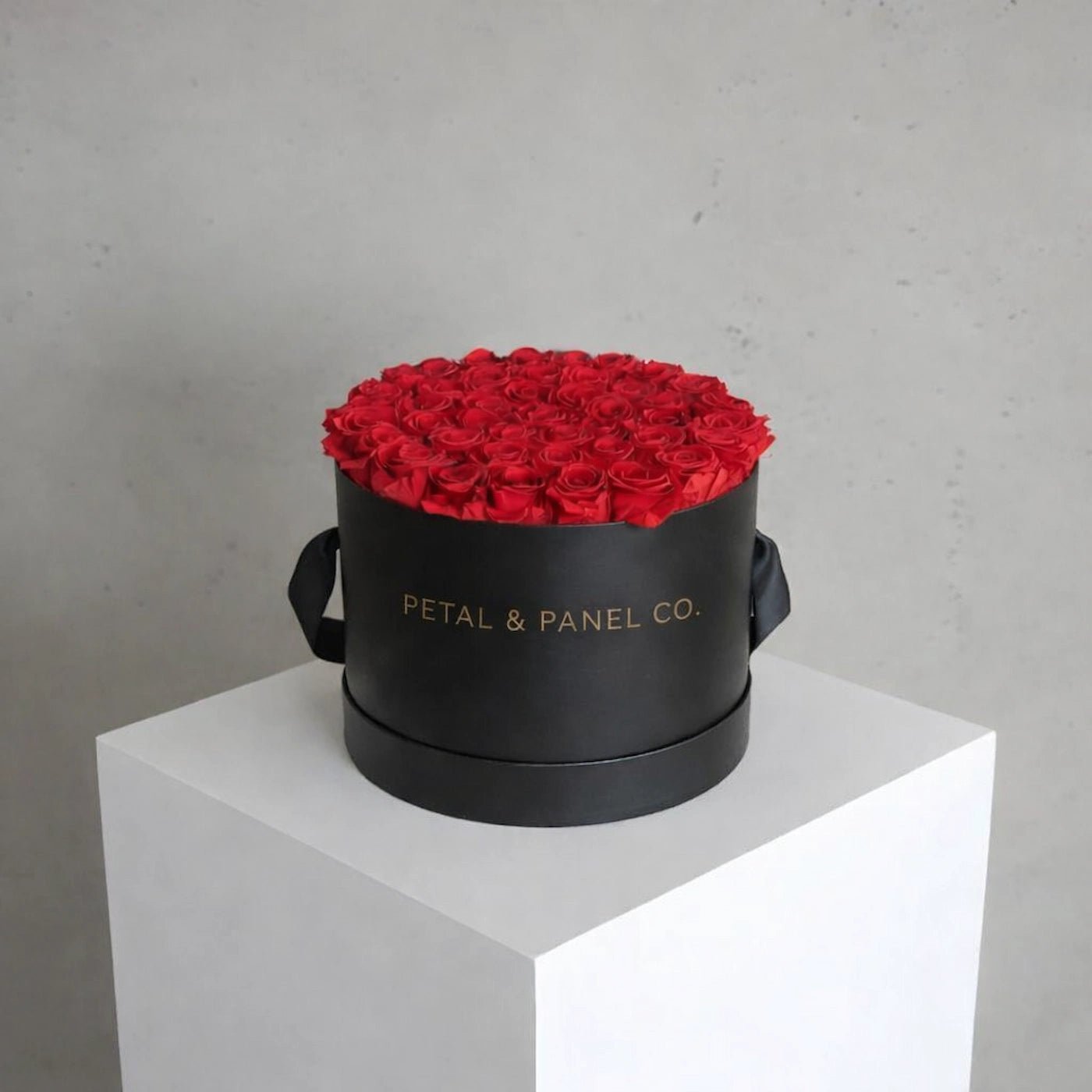 Black round box with red roses on a white pedestal against a gray background