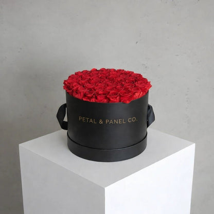 Black round box with red roses on a white pedestal against a gray background