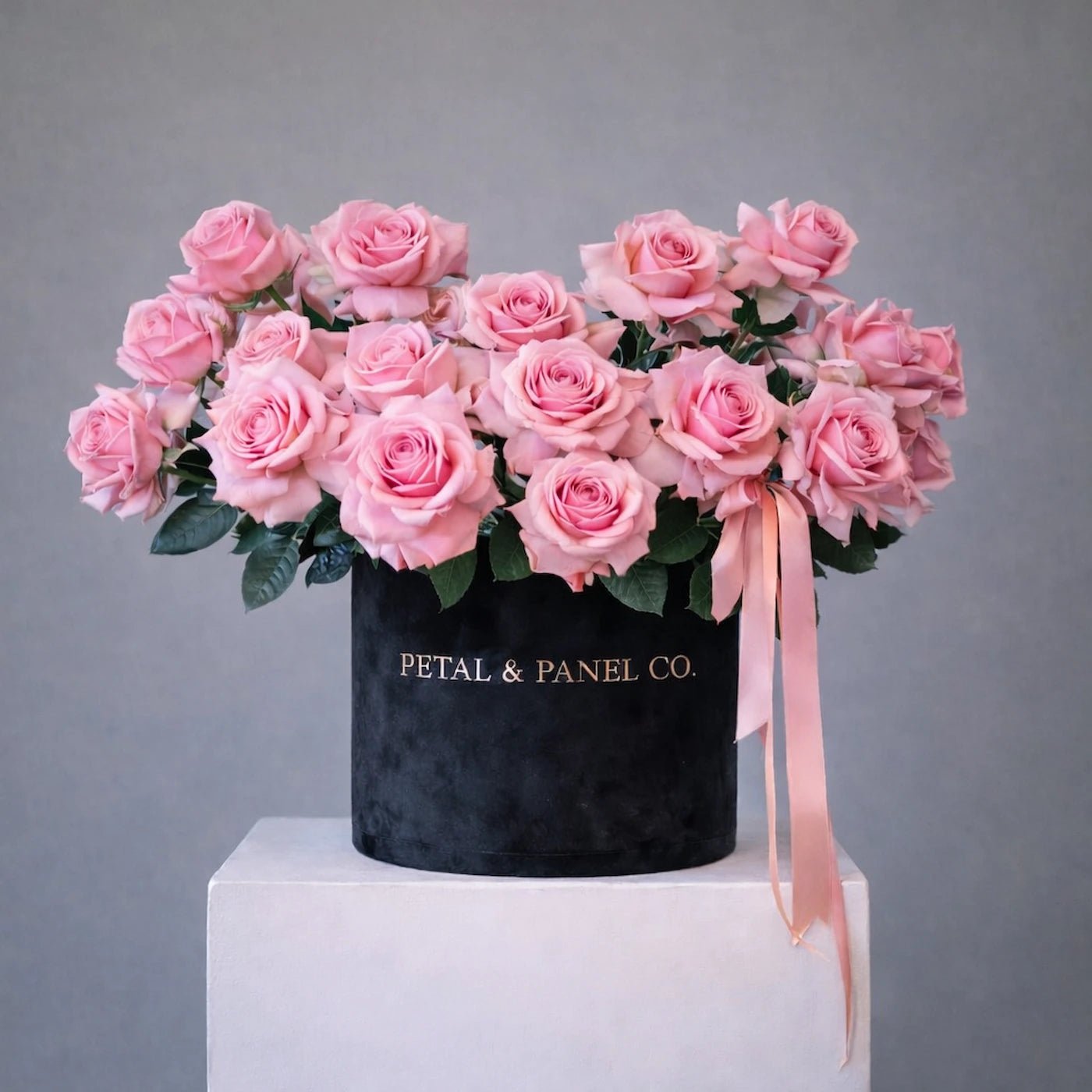 Bouquet of pink roses in a black box with 'Petal & Panel Co.' branding on a gray background.