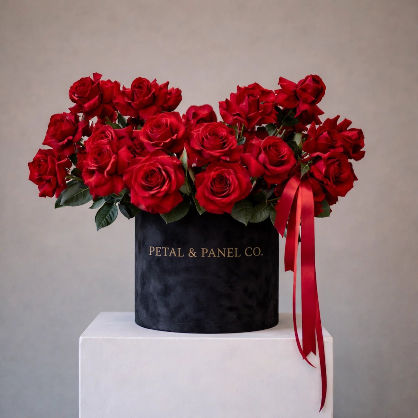Bouquet of red roses in a black box with a red ribbon on a gray background