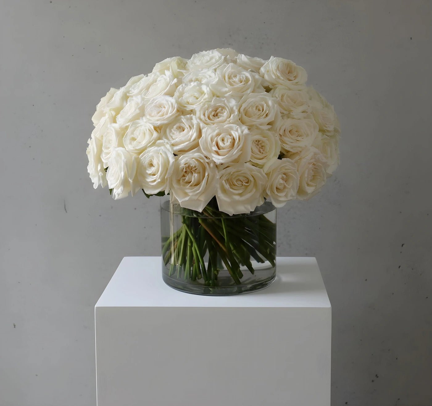 Bouquet of white roses in a clear vase on a white pedestal against a gray background