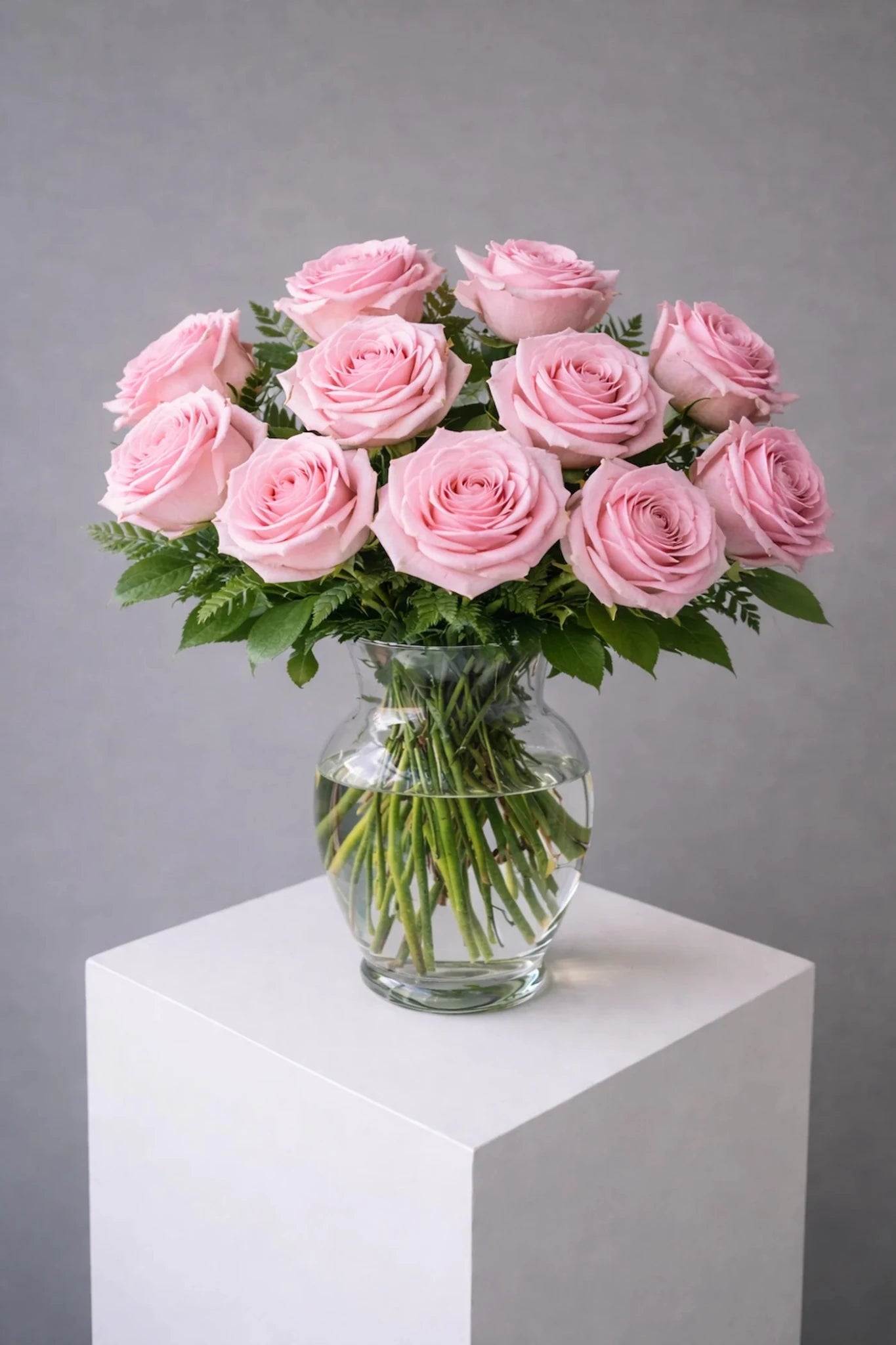 Bouquet of pink roses in a clear vase on a white pedestal against a gray background