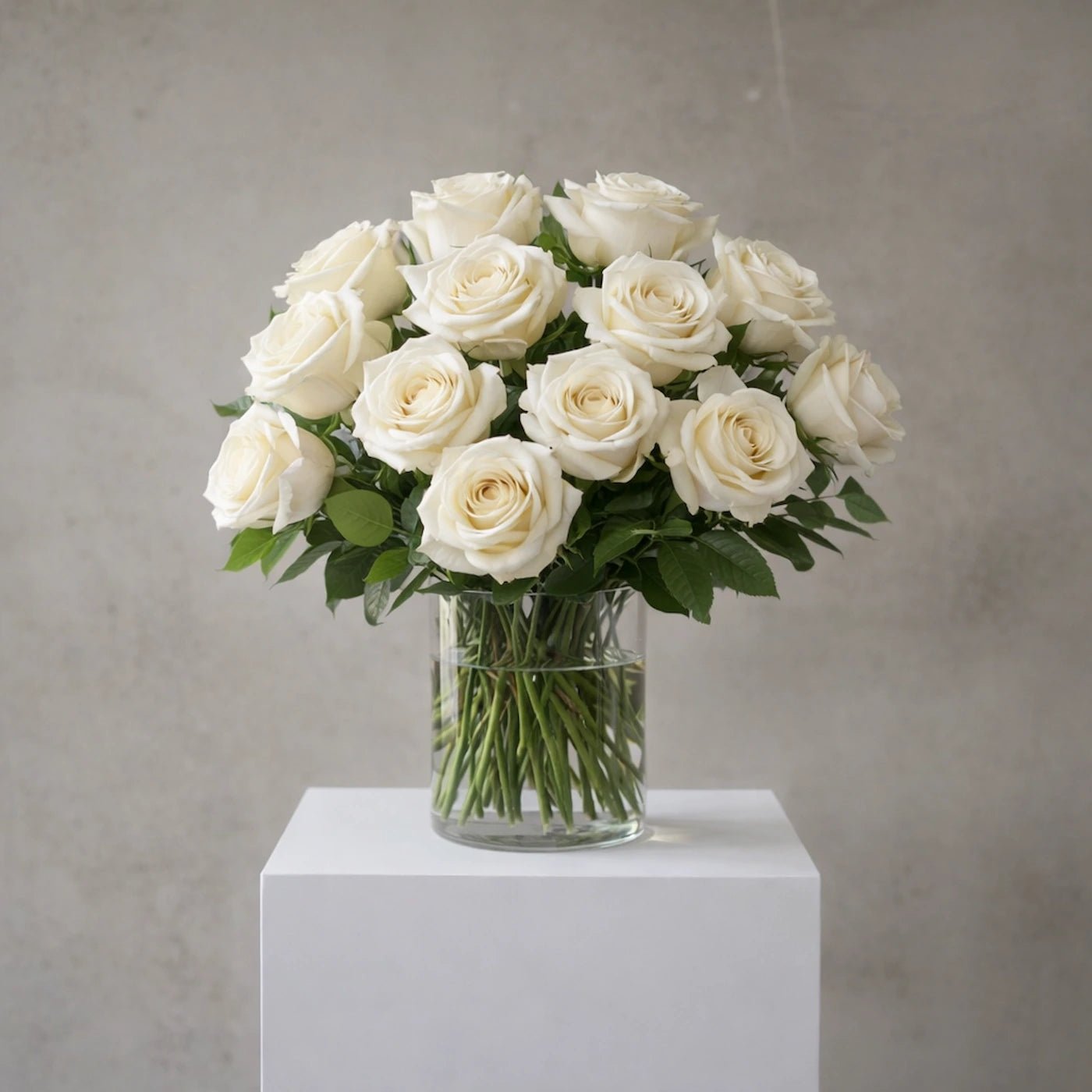 Bouquet of white roses in a clear vase on a white pedestal against a gray background