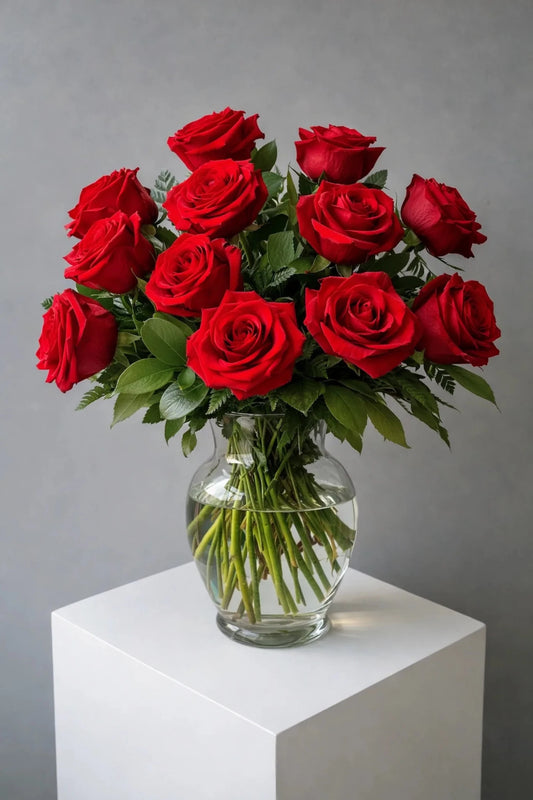 Bouquet of red roses in a clear vase on a white pedestal against a gray background