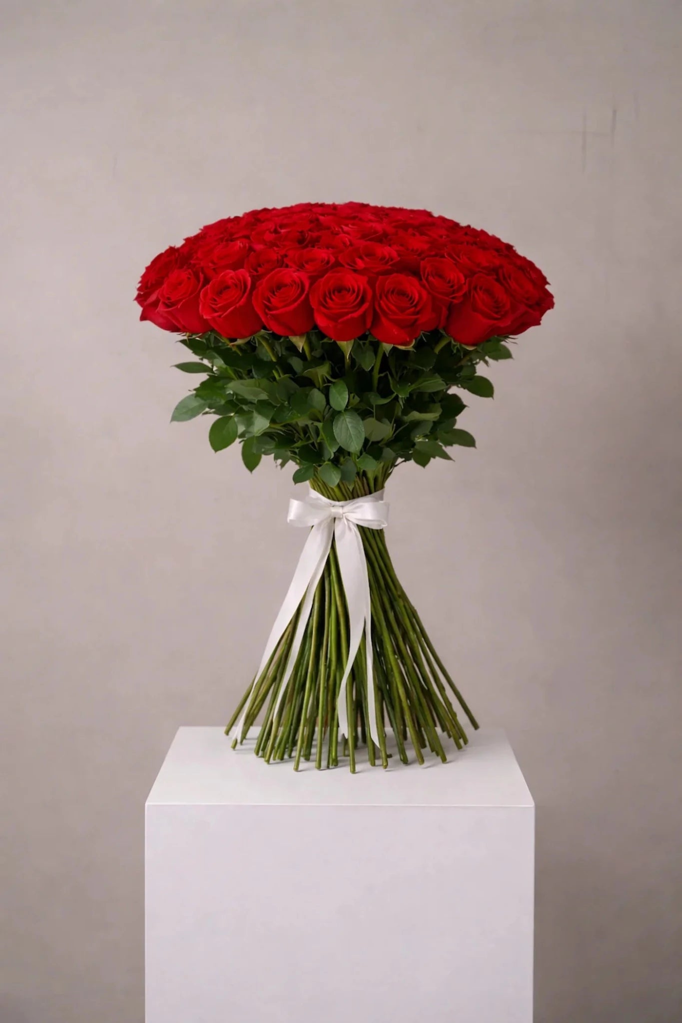 Bouquet of red roses on a white pedestal against a gray background
