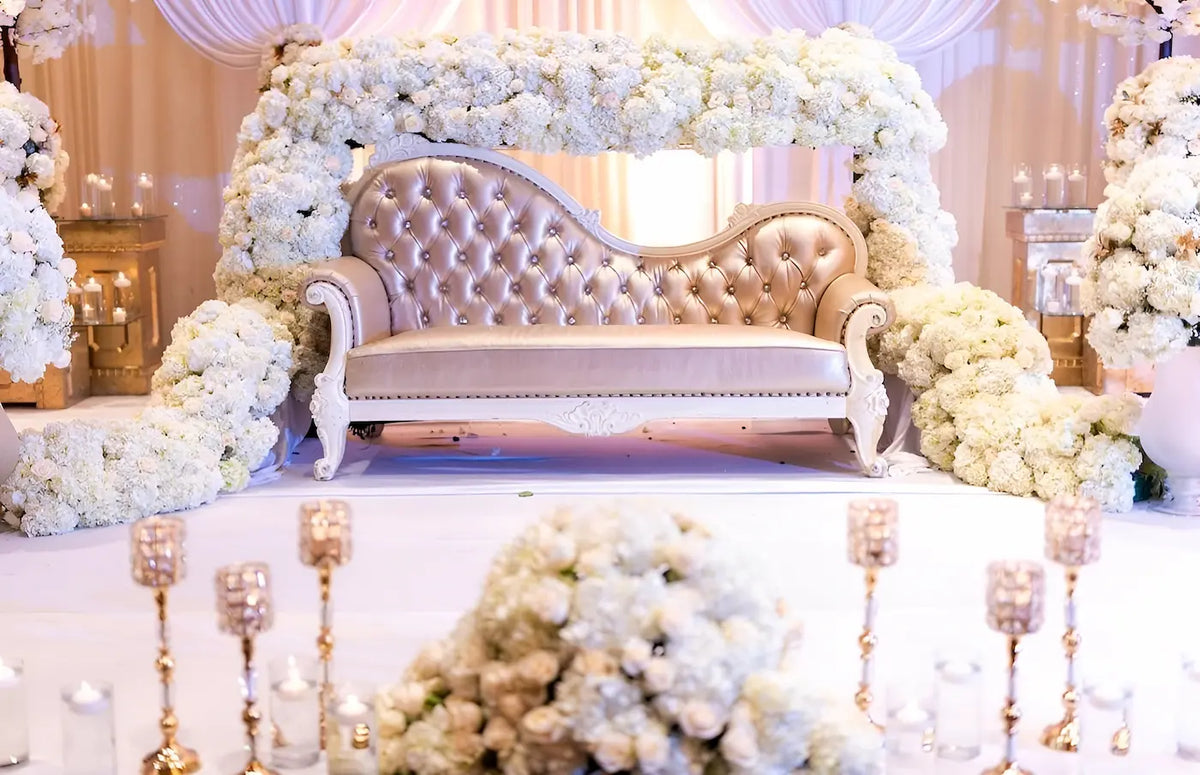 Decorative setup with a white couch surrounded by floral arrangements and candles.