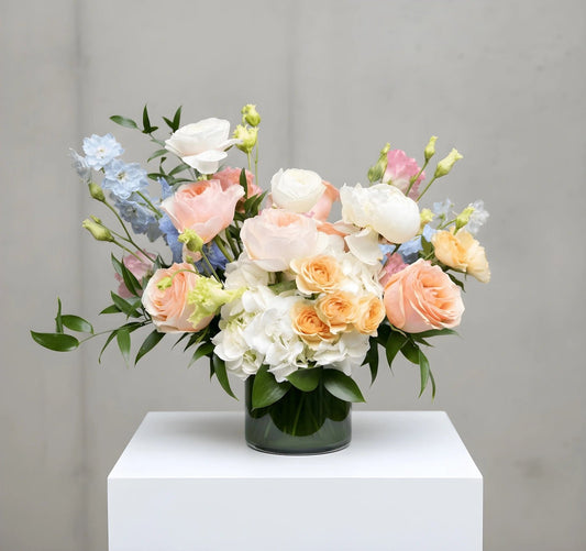 Floral arrangement in a clear vase on a white pedestal against a gray background