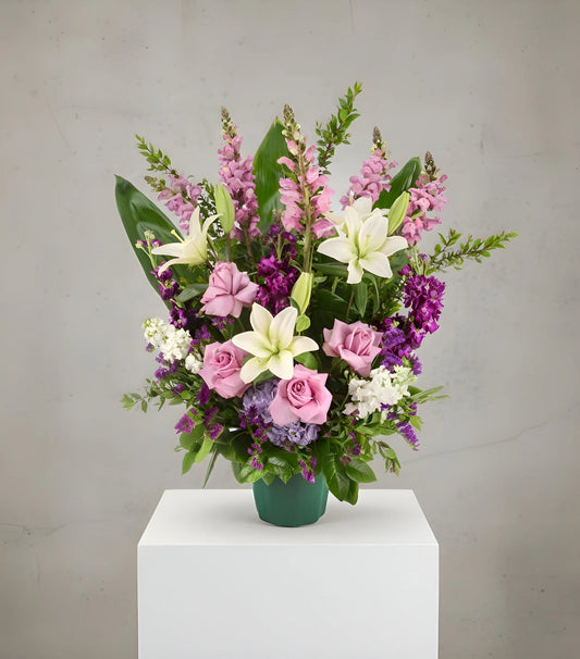 Colorful flower arrangement in a green vase on a white pedestal against a gray background