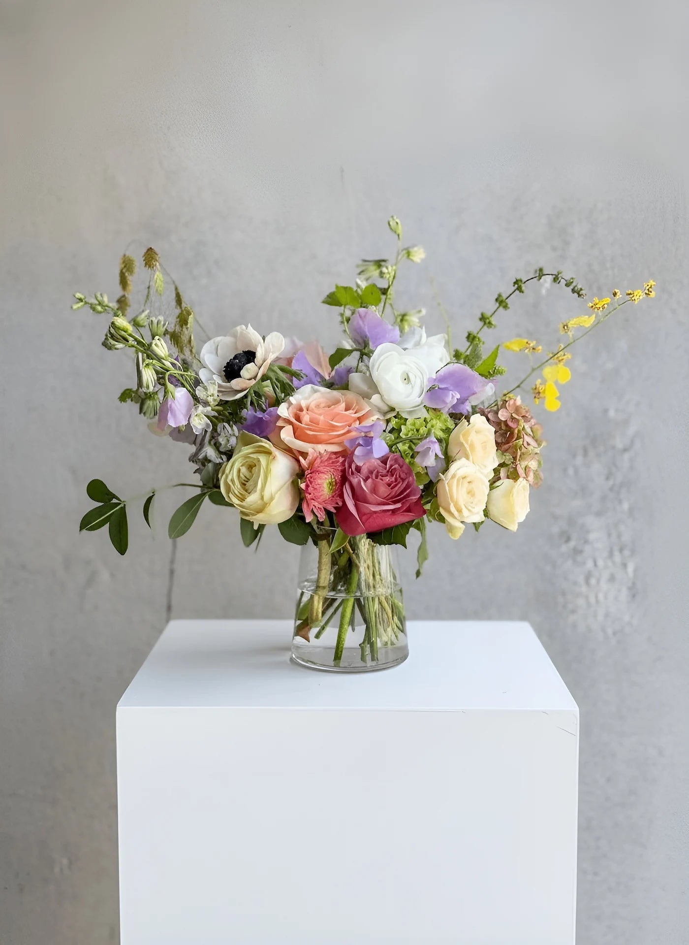 Bouquet of flowers in a clear vase on a white pedestal against a gray background