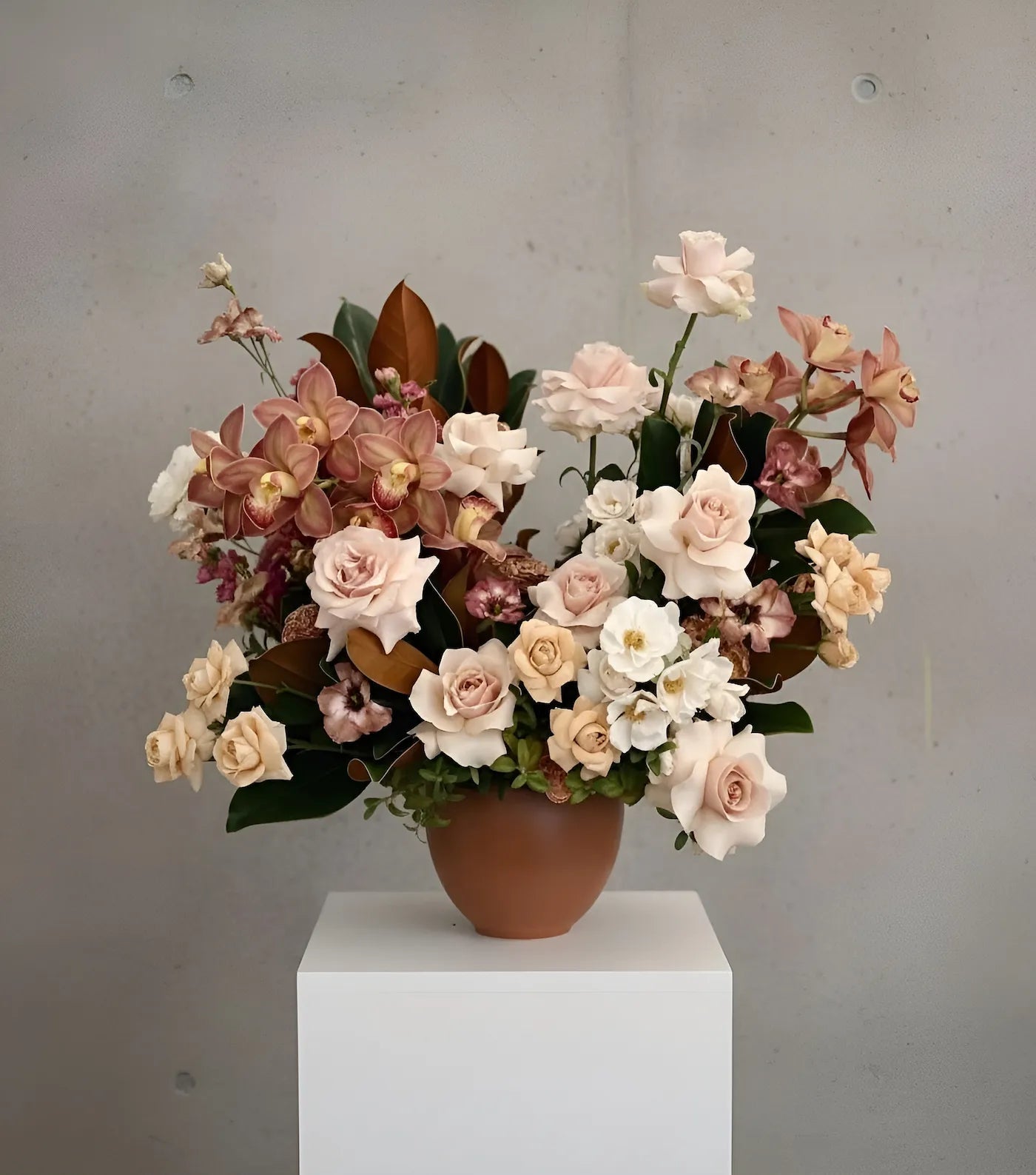 Bouquet of flowers in a terracotta pot on a white pedestal against a gray background