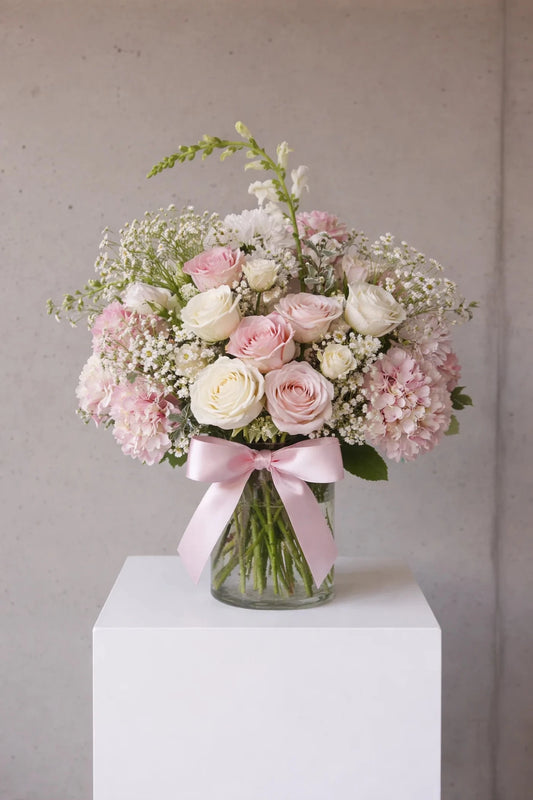 Bouquet of pink and white flowers in a clear vase on a white pedestal against a gray background